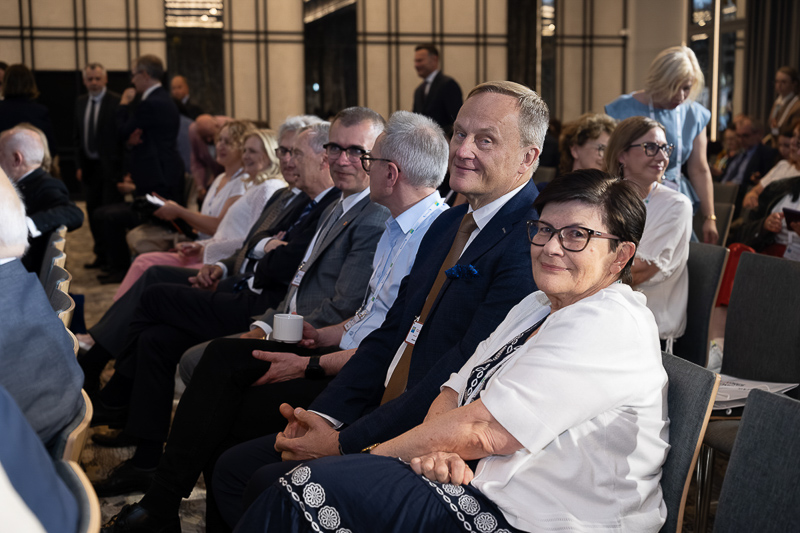 Uczestnicy konferencji siedzący na sali wykładowej i uśmiechnięci do zdjęcia